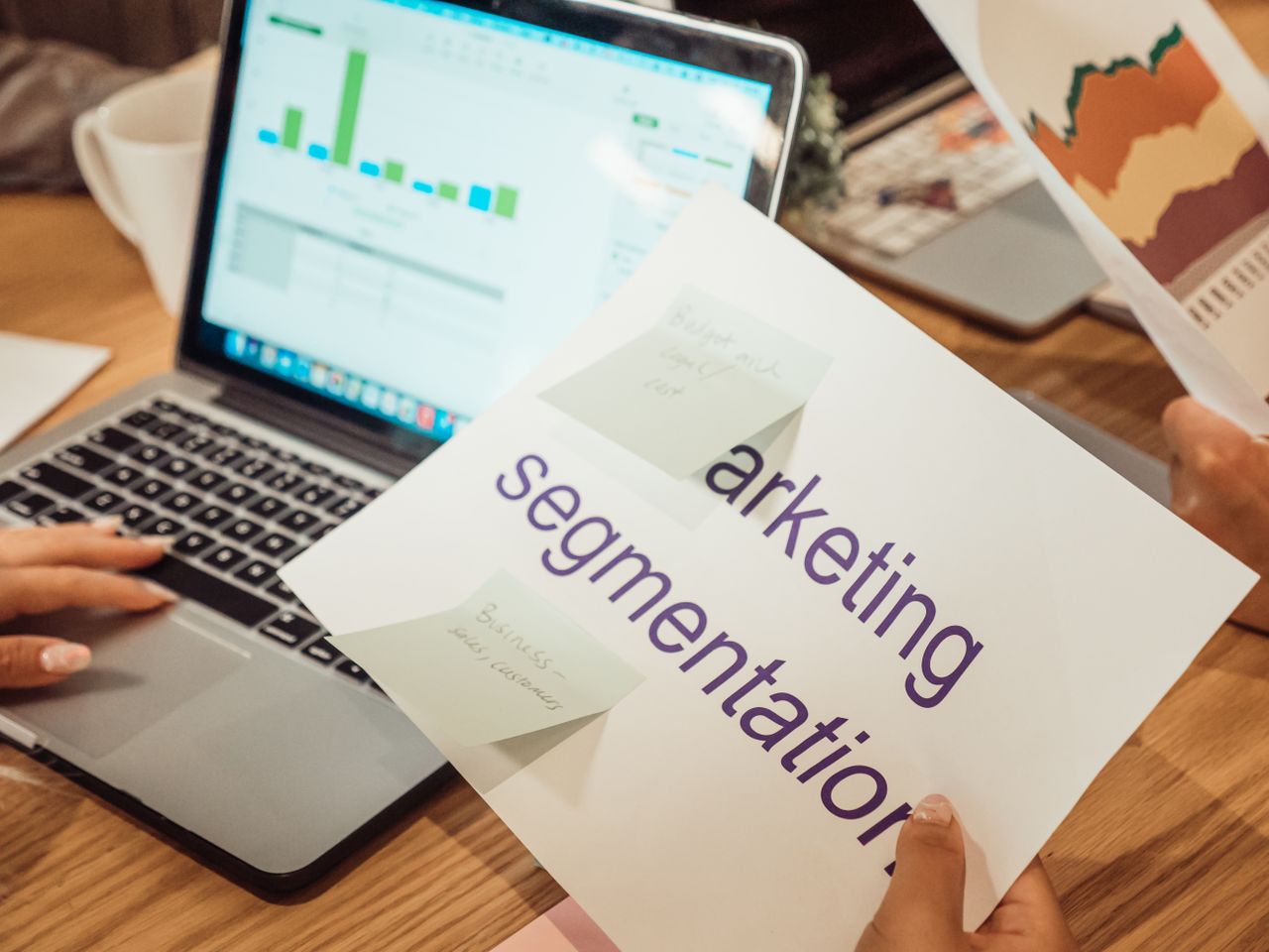 Un espace de travail contemporain où l’on voit des mains analyser des données marketing sur un ordinateur portable et des documents papier.